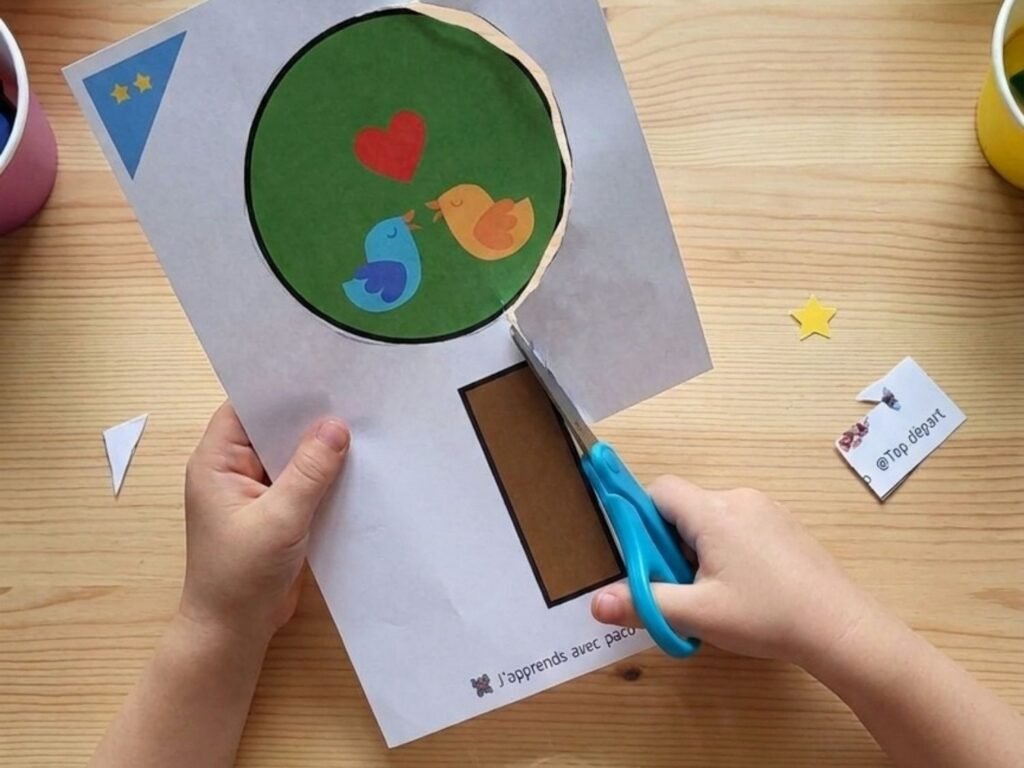 Mains d'un enfant découpant au ciseau le contour circulaire du feuillage d'un arbre sur une fiche imprimée.