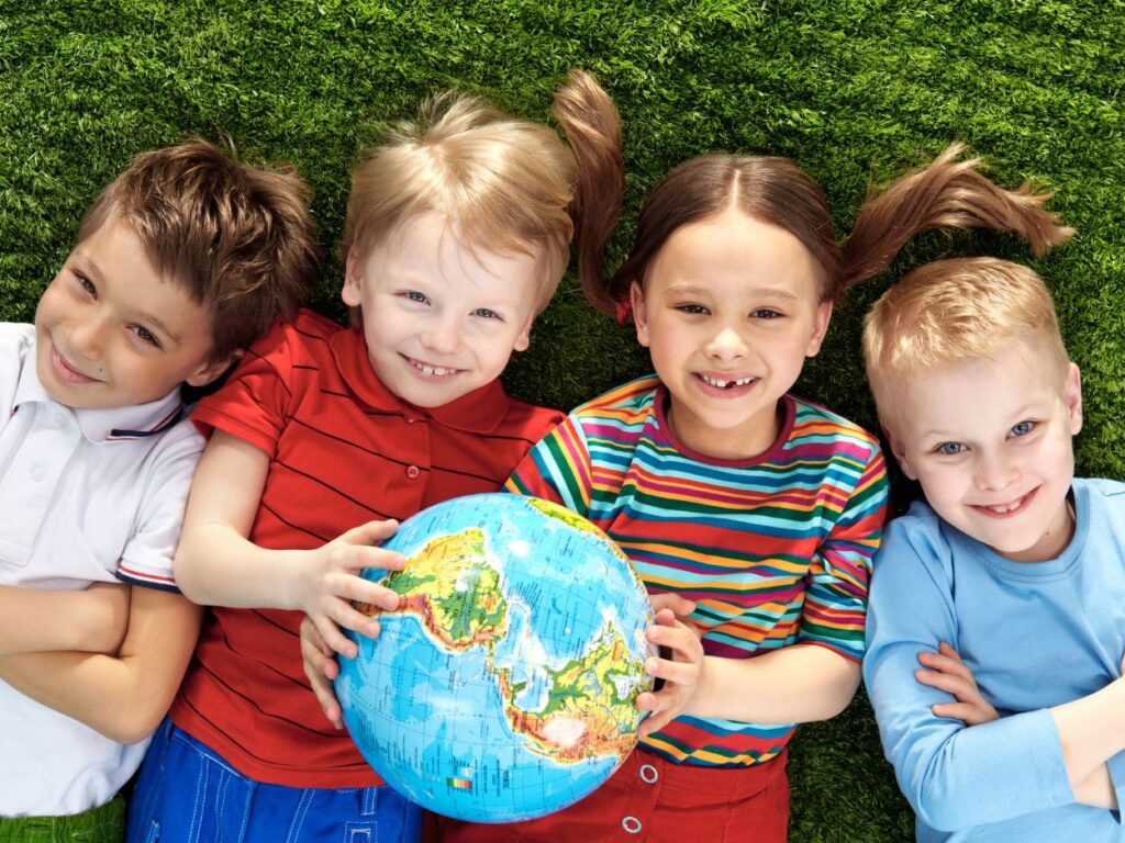 Enfants souriants couchés sur l'herbe tenant un globe terrestre pour découvrir la géographie et les continents.
