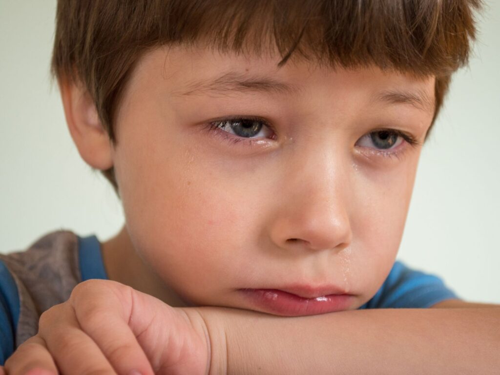 Gros plan sur le visage d'un jeune garçon en larmes, illustrant la tristesse, l'une des six émotions fondamentales de l'enfant.