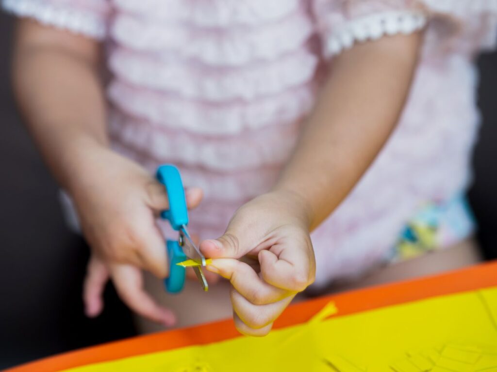 Gros plan sur les mains d'un enfant apprenant à découper une feuille avec des ciseaux.