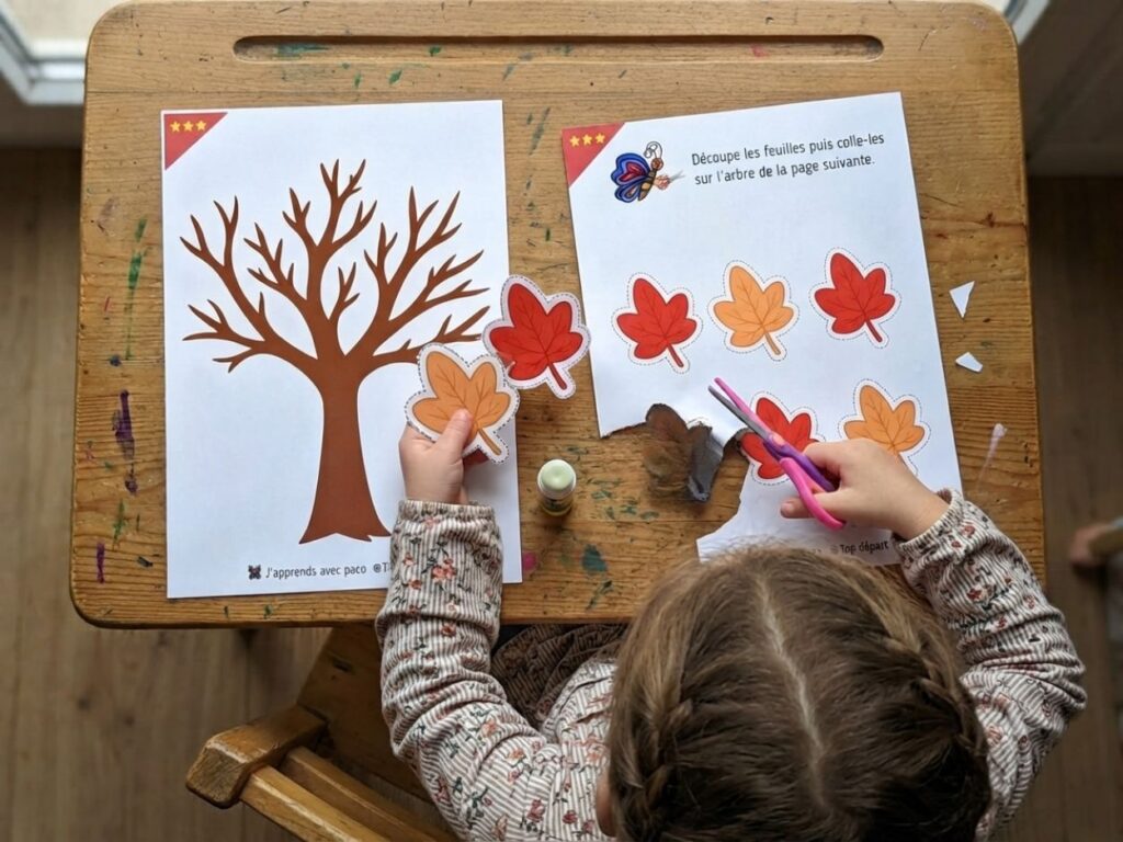 Enfant de maternelle réalisant un exercice de découpage et collage de feuilles d'automne