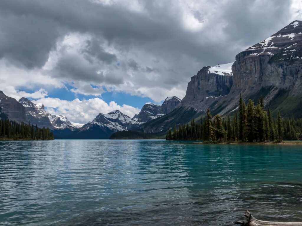 Lac aux eaux turquoise entouré de montagnes escarpées et de forêts sous un ciel nuageux.