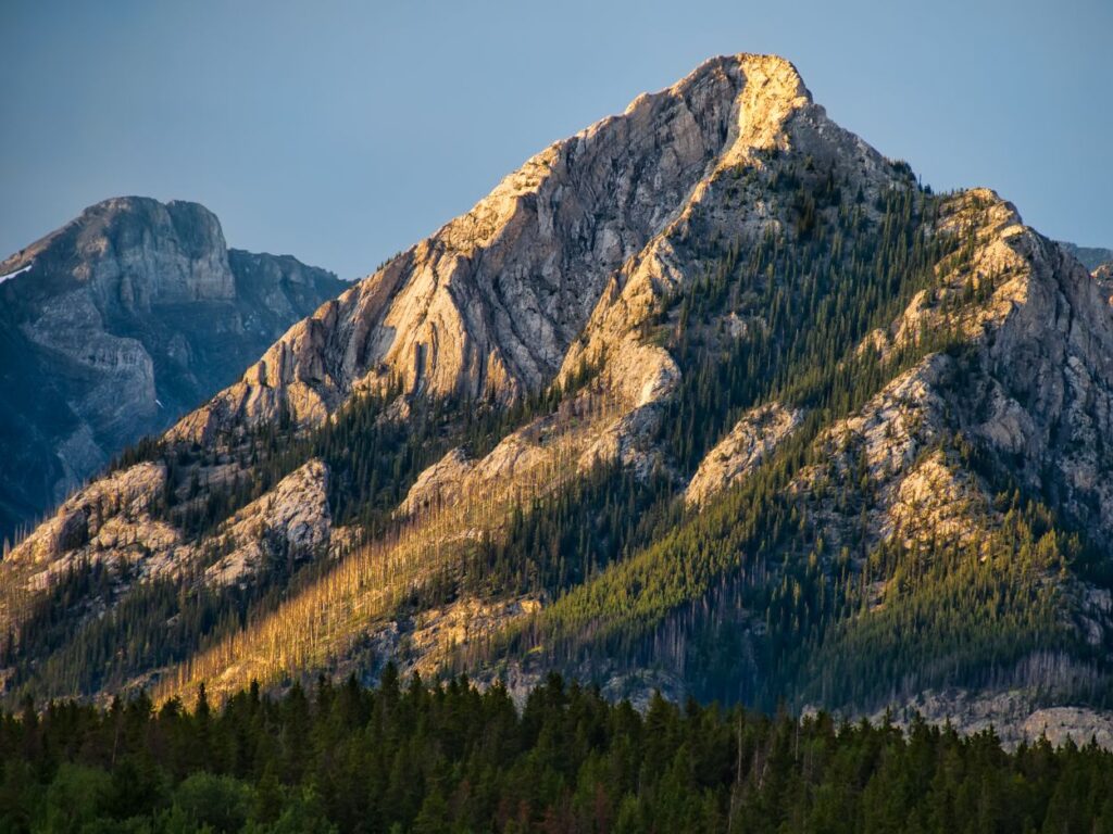 Sommet rocheux illuminé par la lumière dorée du coucher du soleil avec une forêt au premier plan.