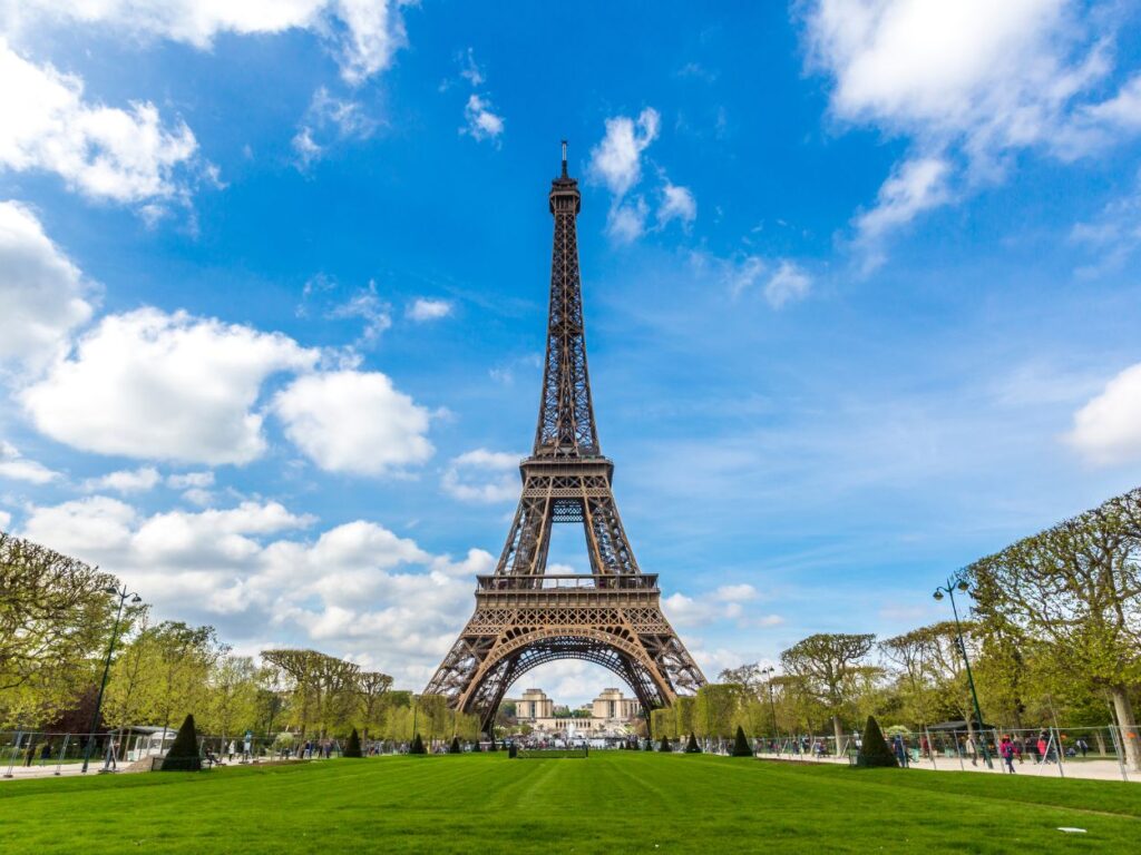 Vue de la tour Eiffel à Paris sous un ciel bleu avec des nuages.